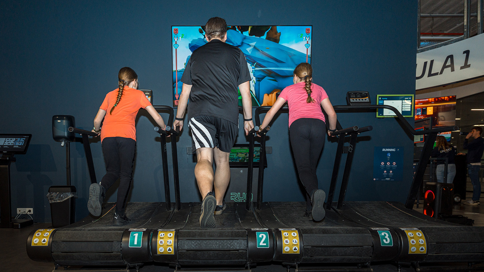 Drie lopers op de exergaming-loopbanden voor een groot scherm